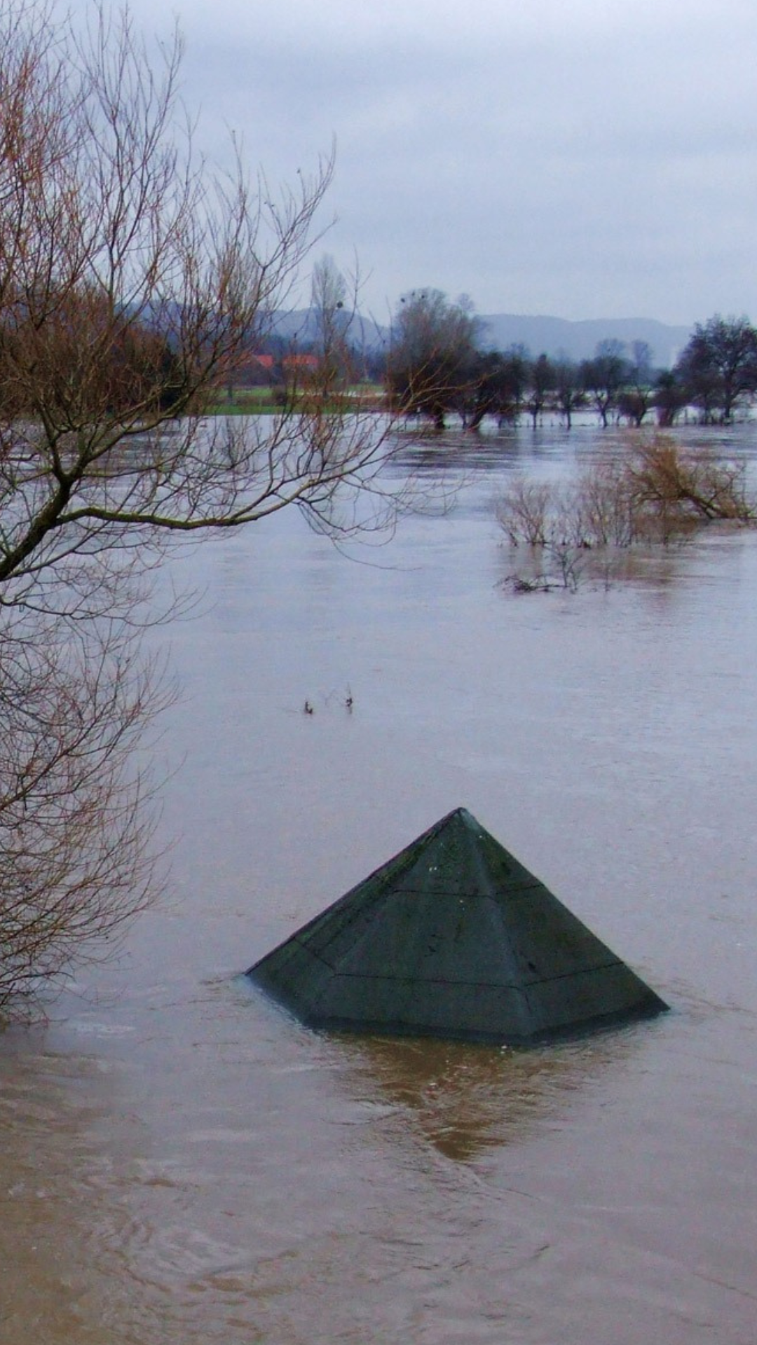 The roof of a house surrounded by brown flood waters sticks up above the water line.